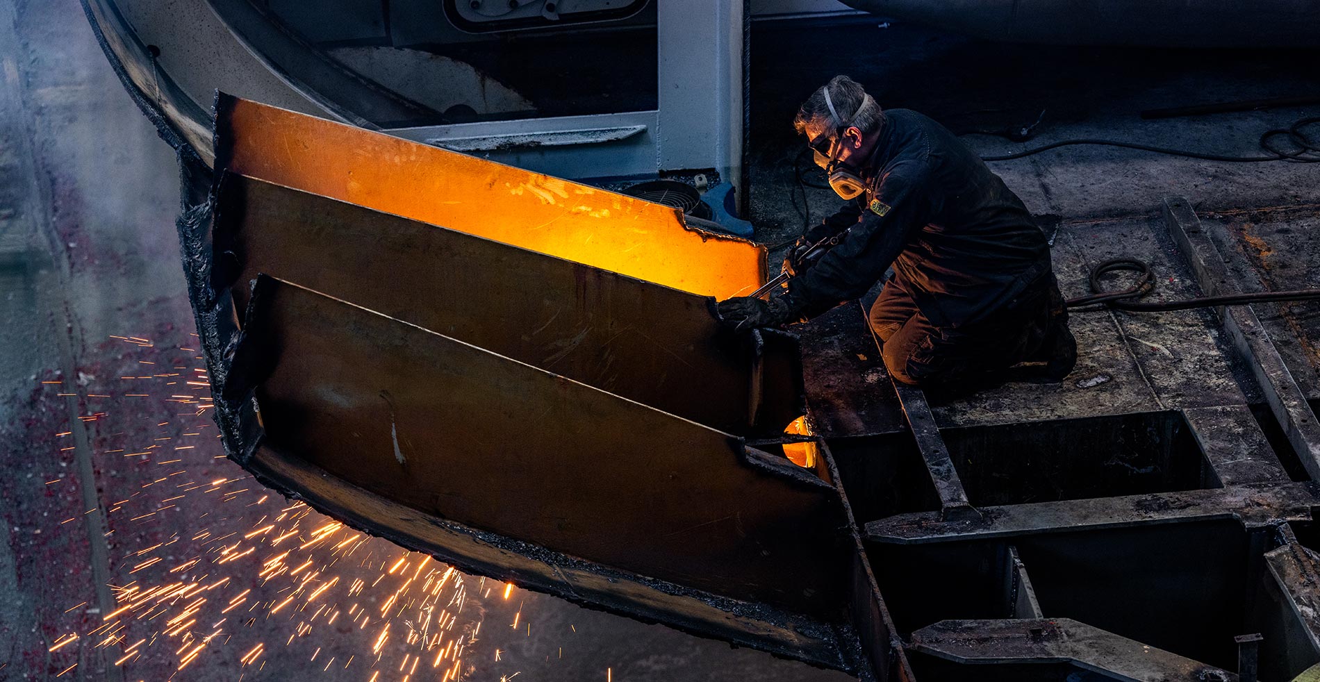 Welder cutting steel in the shipyard, sparks and glowing metal